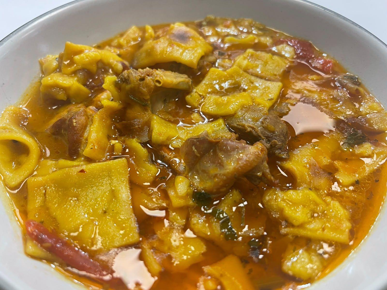 Plato de pasta con salsa dorada y trozos de carne en un bol blanco