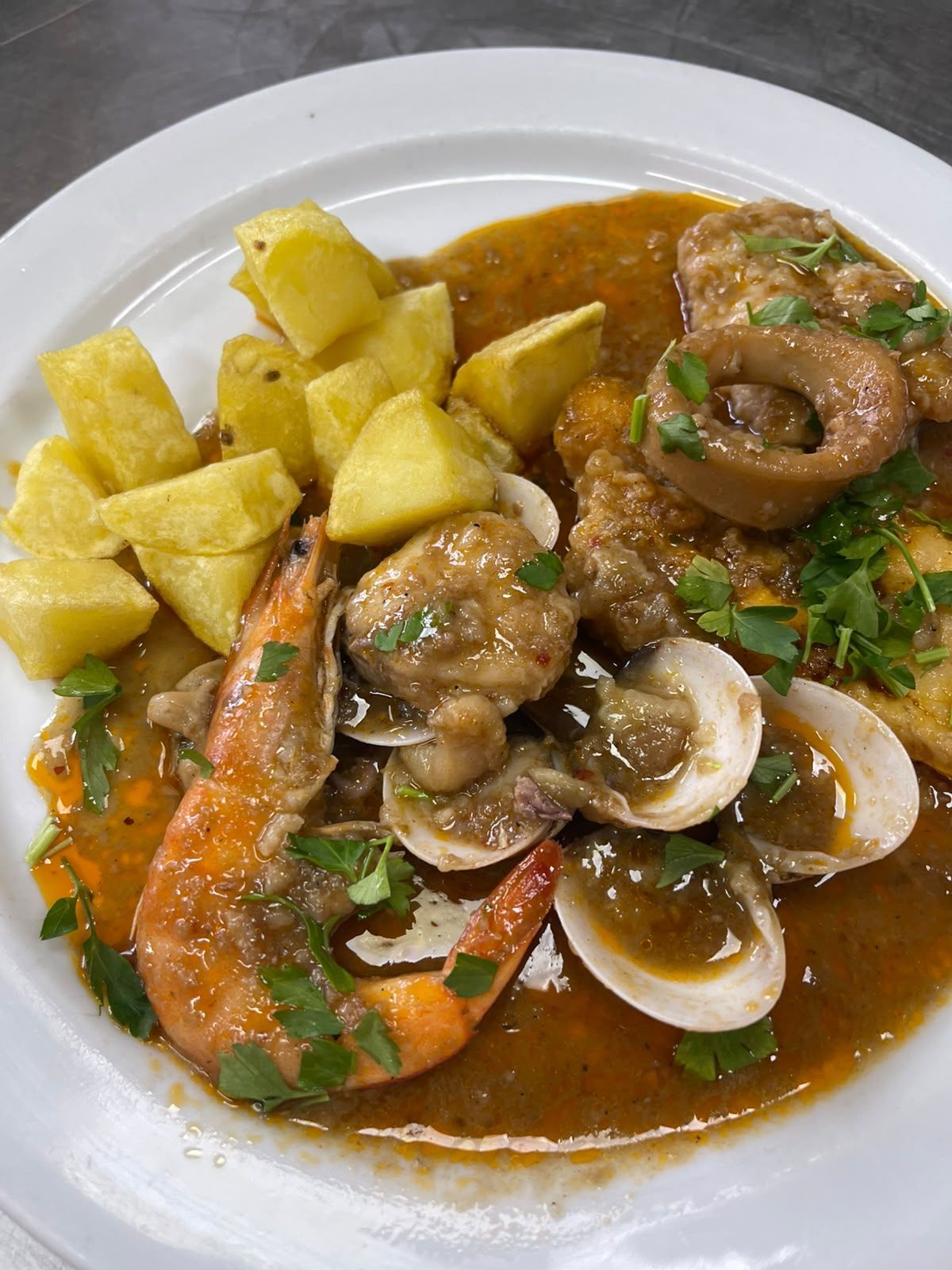 Guiso de mariscos con almejas, camarones y patatas en salsa marrón en un plato blanco