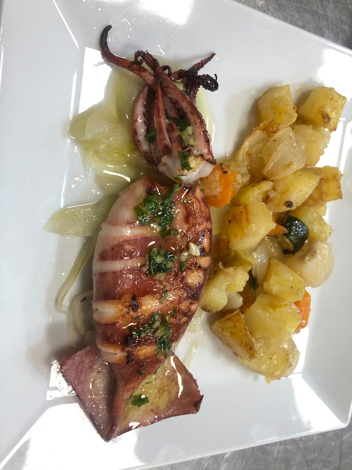 Pulpo a la parrilla con patatas en un plato blanco, cubierto de hierbas y salsa