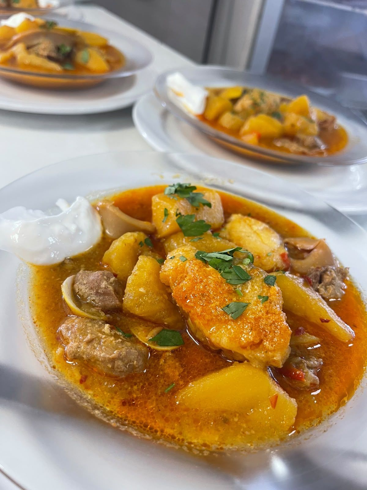 Tres cuencos de contundente guiso de patatas y carne, adornados con hierbas y servidos sobre un mantel blanco