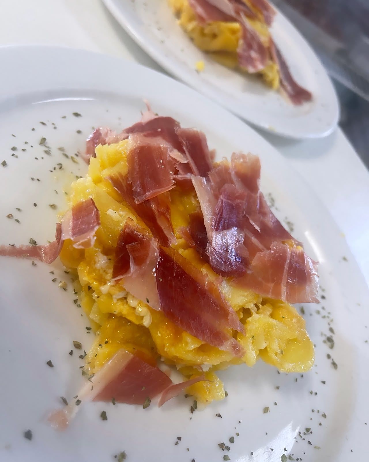 Risotto emplatado con prosciutto y hierbas, con otro plato al fondo