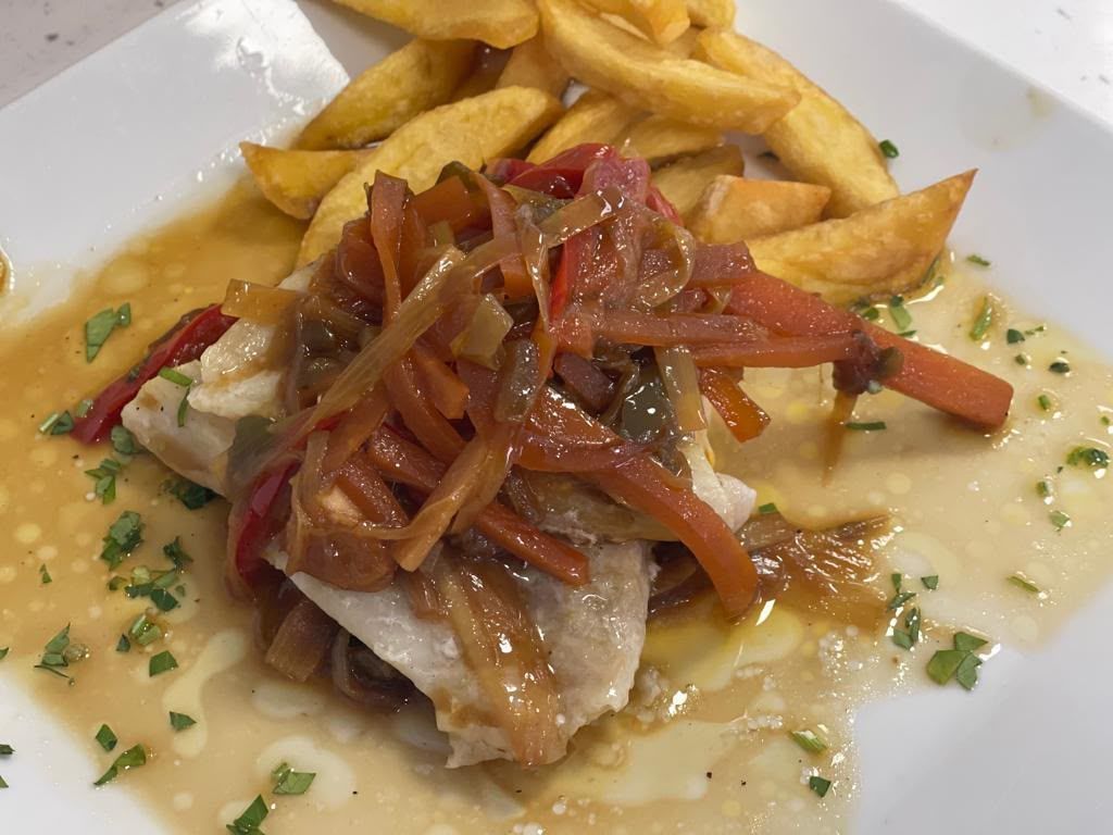 Plato de pescado frito con cebolla y pimientos salteados, acompañado de patatas fritas gruesas y salsa cremosa