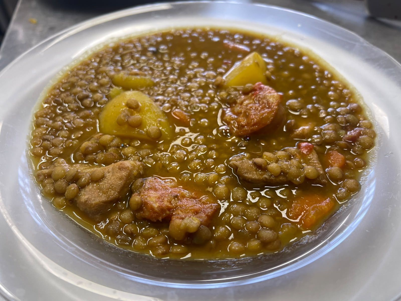 Cuenco de guiso espeso de lentejas marrones con trozos de carne y patatas en un plato blanco