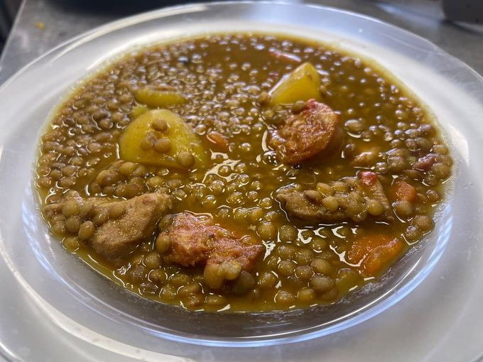 Cuenco de guiso espeso de lentejas marrones con trozos de carne y patatas en un plato blanco