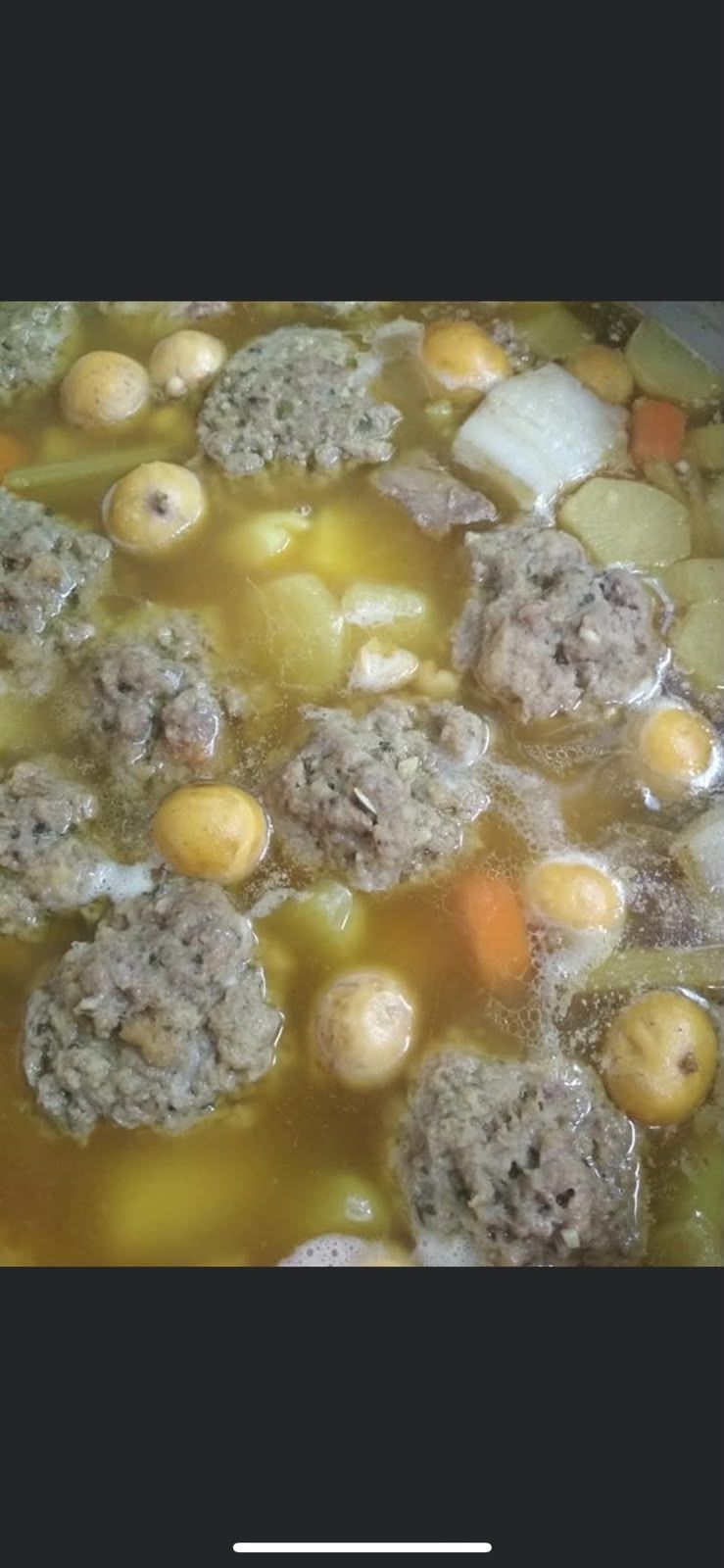 Albóndigas, patatas y verduras cocinándose a fuego lento en un caldo amarillo dentro de una olla
