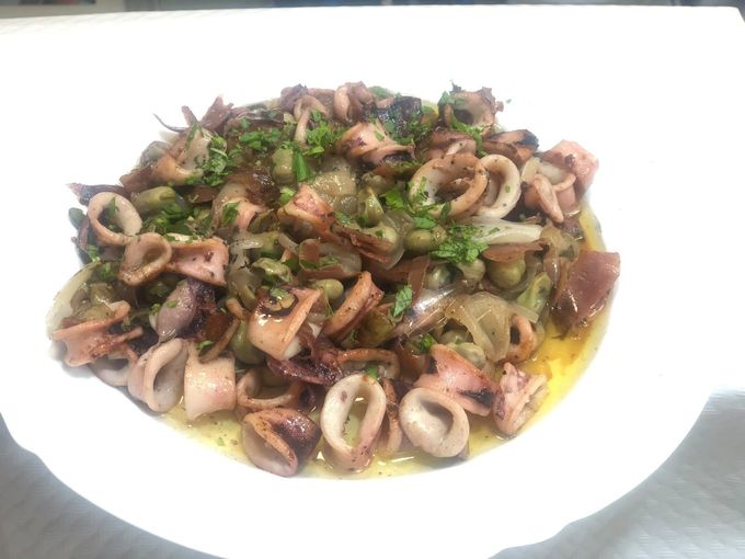 Plato de calamares salteados con hierbas y salsa, servido en un plato blanco
