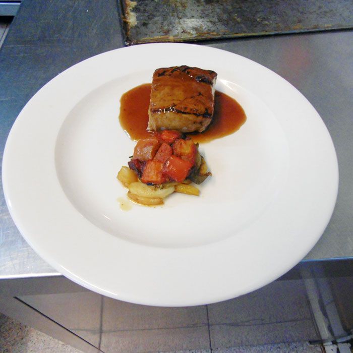 Un plato blanco con un trozo de carne y verduras encima.