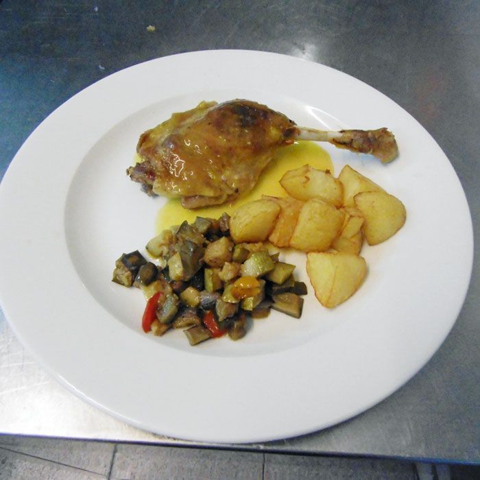 Un plato blanco con una pierna de pollo y patatas encima.