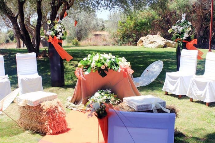 Una mesa con flores está rodeada de sillas y fardos de heno.