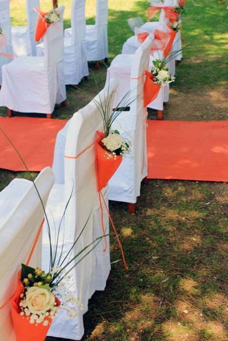 Una fila de sillas blancas con flores naranjas sobre ellas.