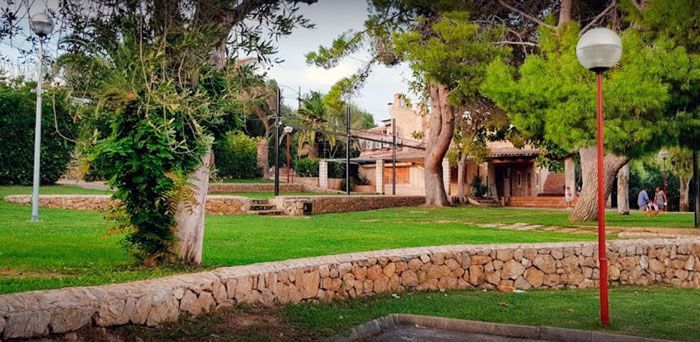 Un parque con un muro de piedra, césped, árboles y un poste rojo.