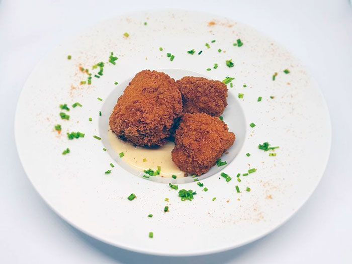 Un plato blanco cubierto con comida frita y salsa sobre una mesa.