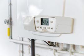 Chaudière à gaz murale blanche avec affichage numérique indiquant 28,4 degrés. Tuyaux visibles.