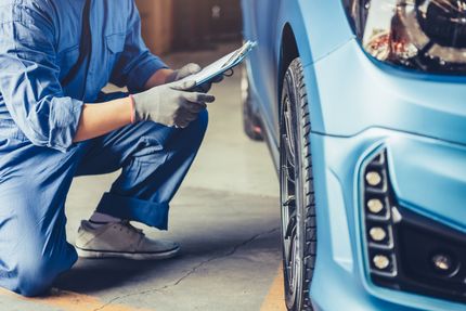 Un mécanicien est agenouillé à côté d'une voiture bleue et regarde une tablette.