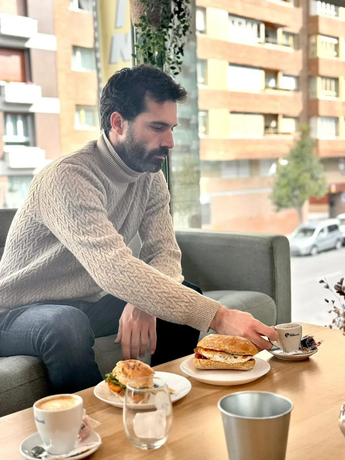 Un hombre está sentado en una mesa con un sándwich y una taza de café.