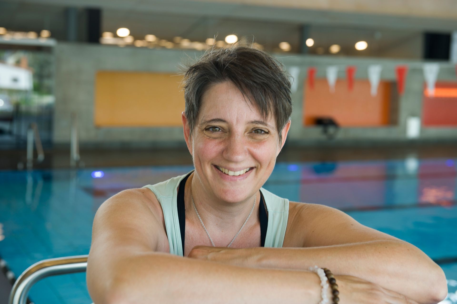 Christine Herholz im Stutenseebad am Beckenrand, sie lächelt in die Kamera, im Hintergrund ist eine bunte Wand zu sehen.