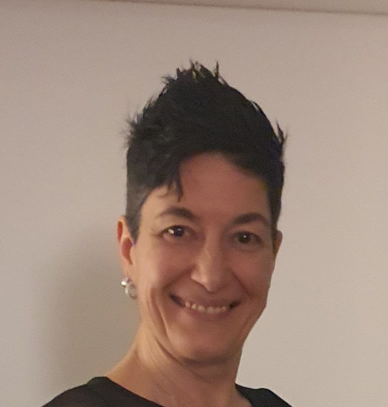 Blonde Frau lächelt in einem weißen Oberteil vor gelbem Hintergrund.