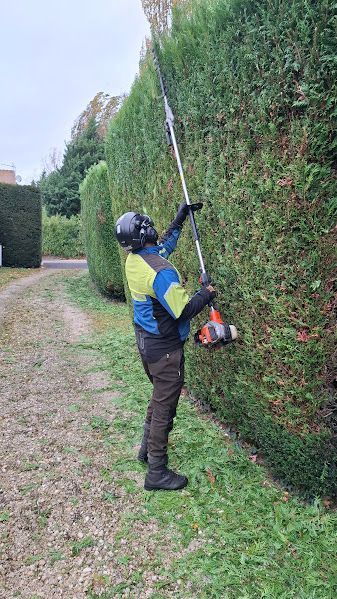 Personne utilisant un sécateur pour tailler une haie verte ; poignées bleues, gants orange.