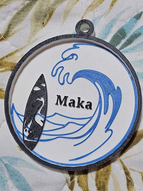 Una medalla con una tabla de surf y el nombre maka en ella