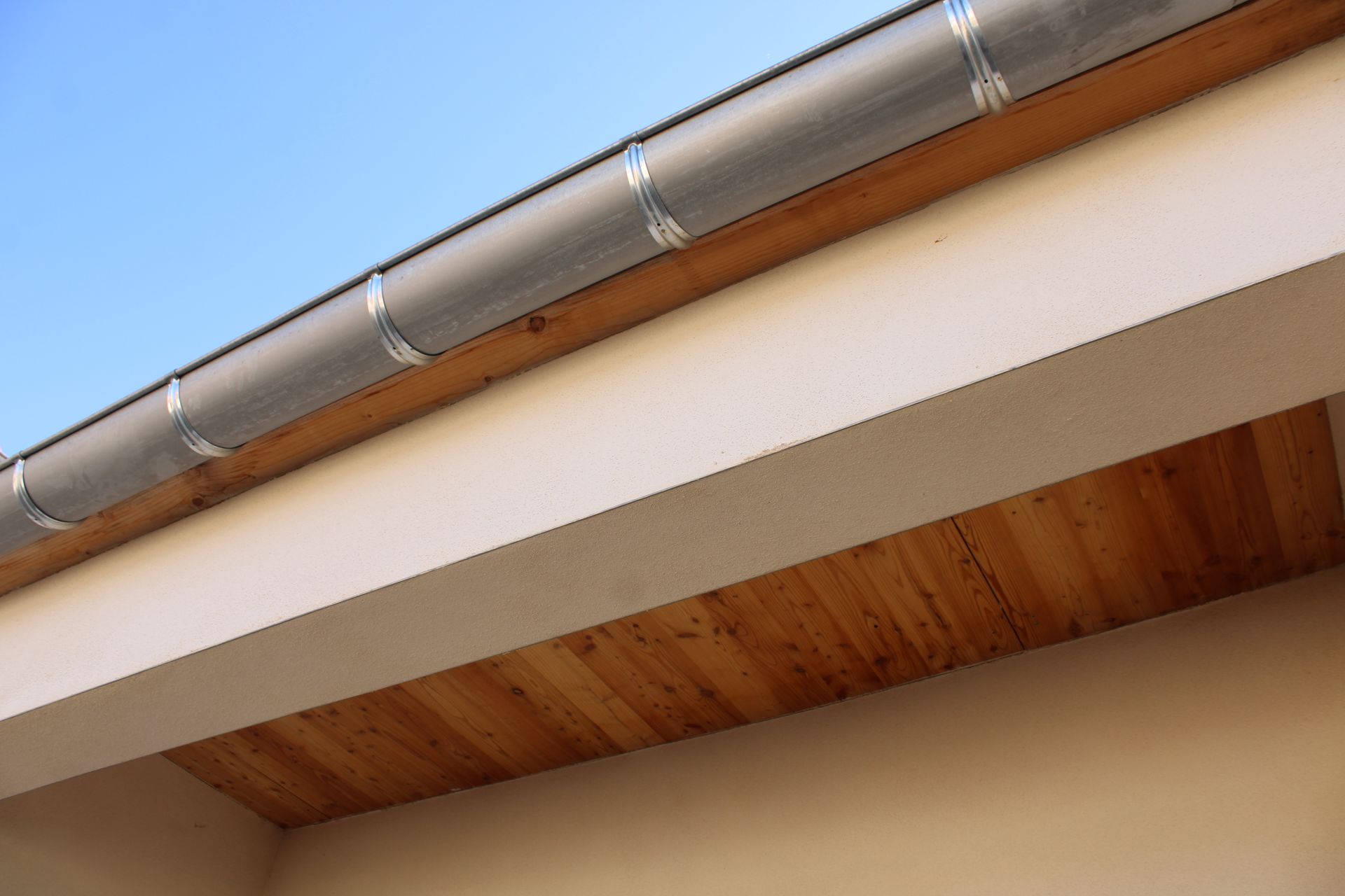 Gouttière grise le long du bord d'un toit, avec un soffite beige et des panneaux de bois en dessous.