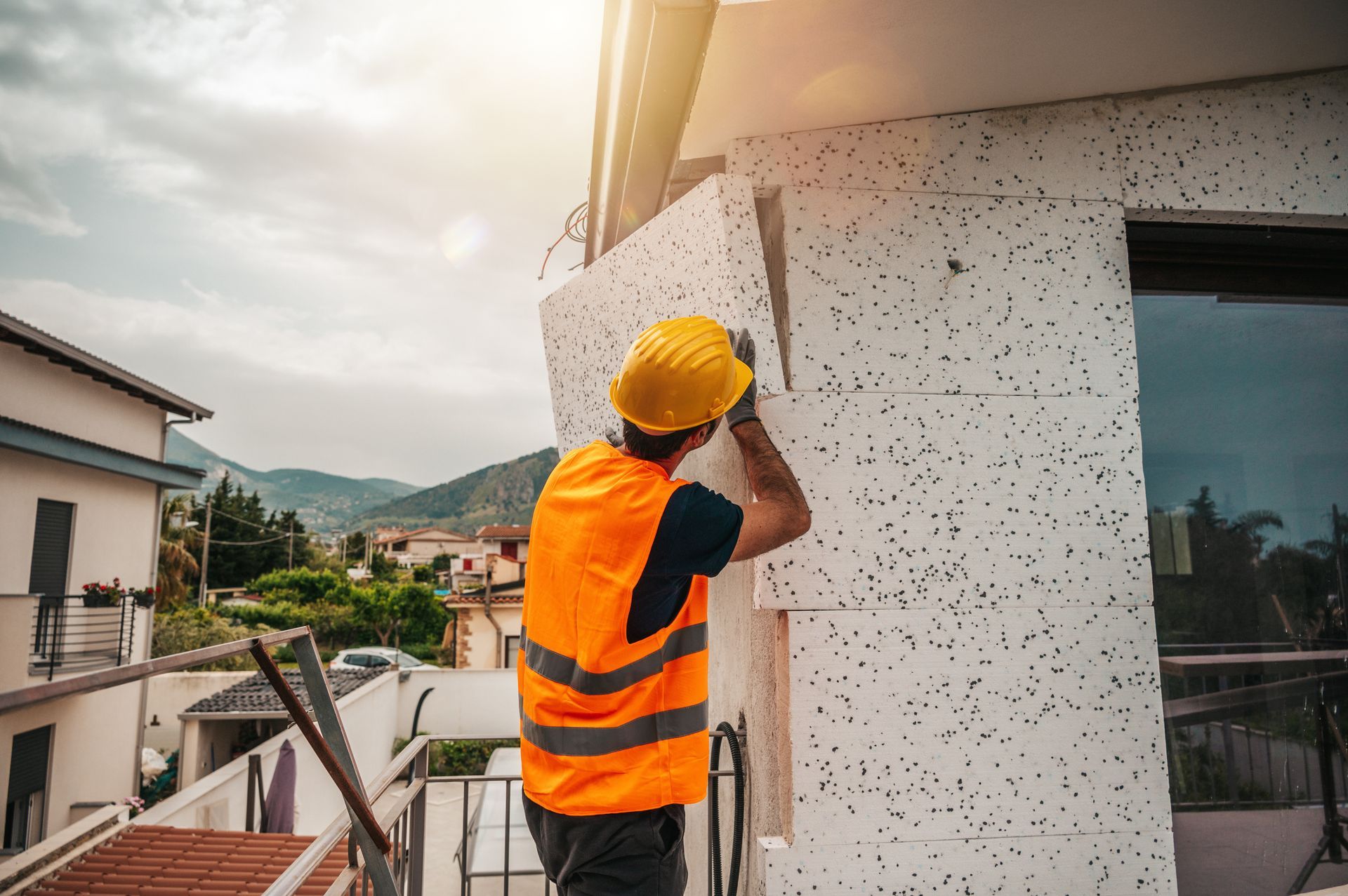 Ouvrier du bâtiment portant un gilet orange et un casque de sécurité installant de l'isolant sur l'extérieur d'un bâtiment.