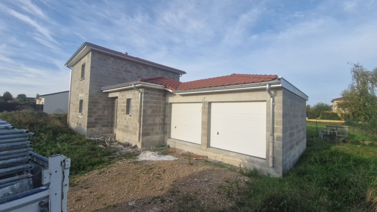 Bâtiment en béton avec portes de garage, toit de tuiles rouges, entouré d'herbe et de ciel.