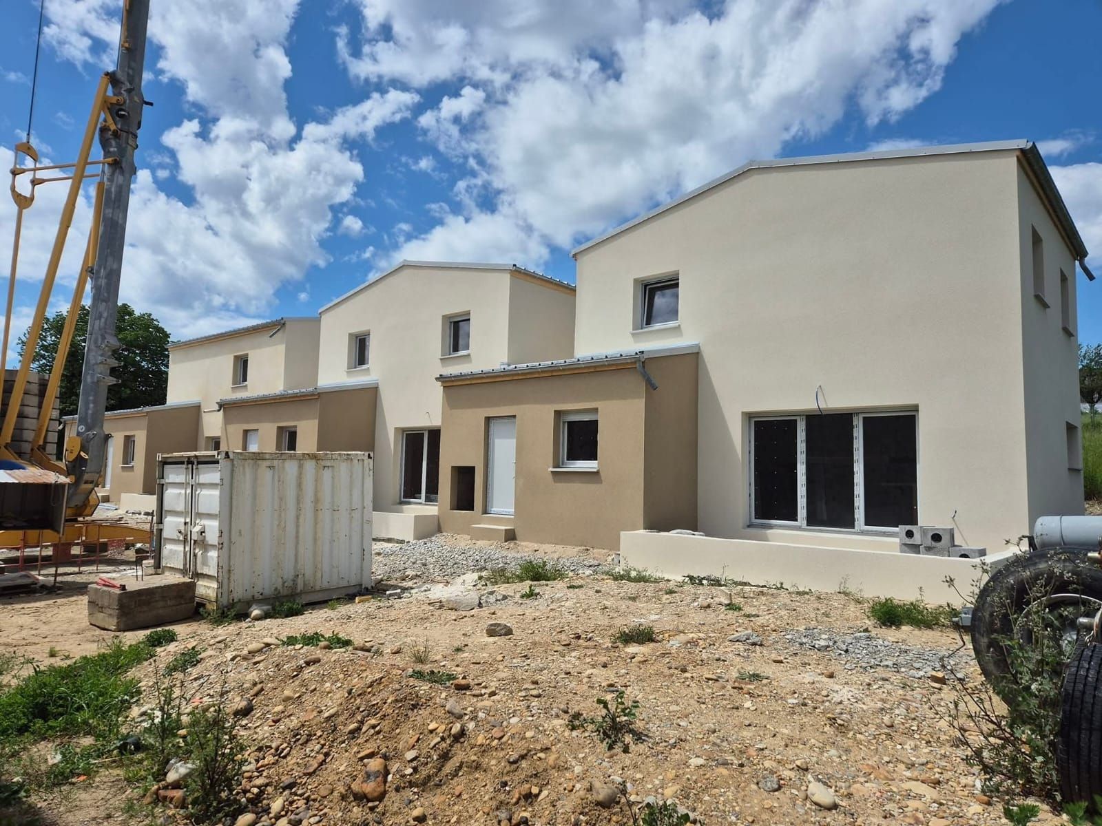 Rangée de maisons beiges et ocre nouvellement construites sous un ciel bleu nuageux ; chantier de construction au premier plan.