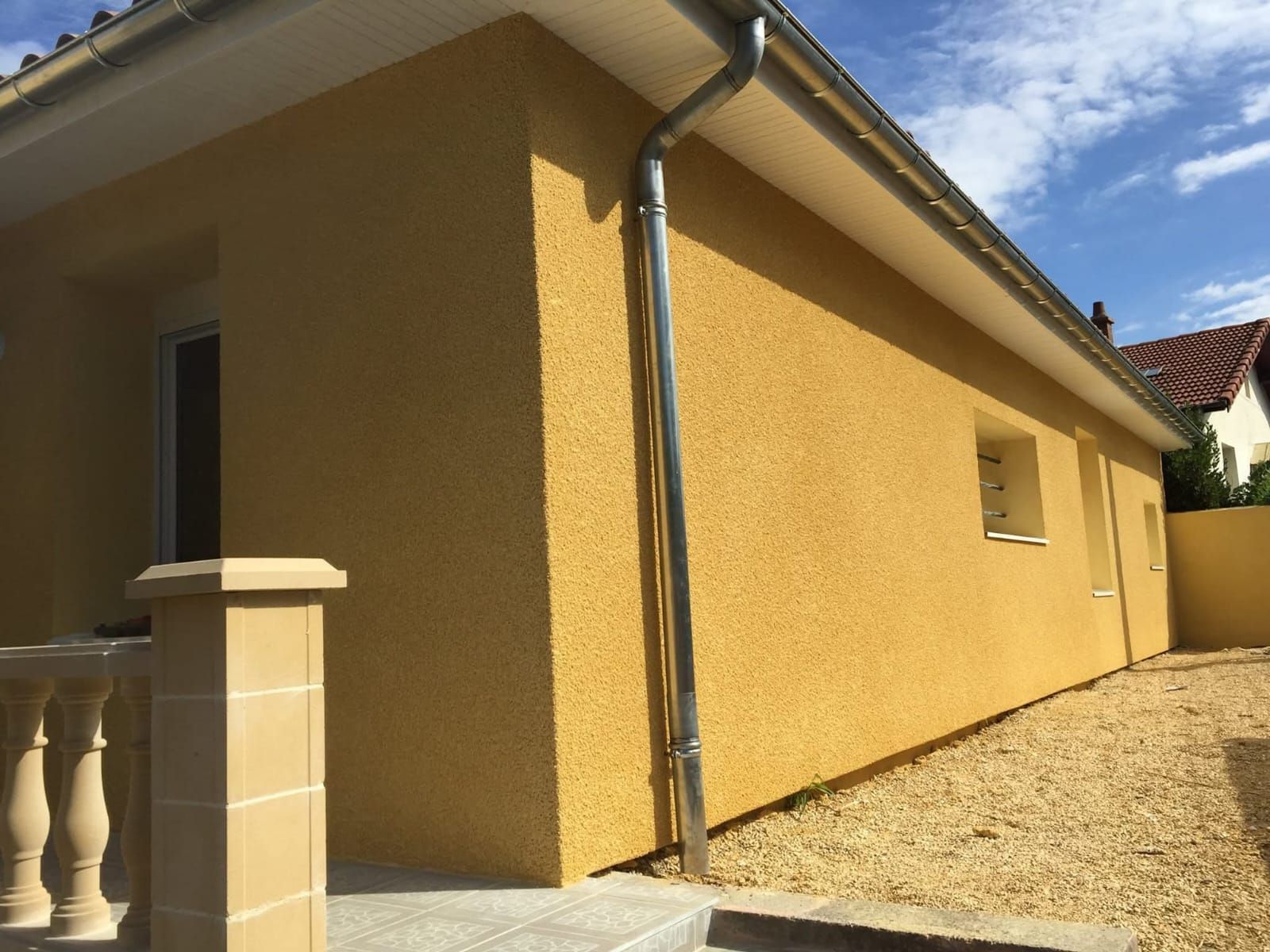 Un homme pulvérise de la peinture blanche sur un mur à l'extérieur, portant un équipement de sécurité ; sous le soleil.