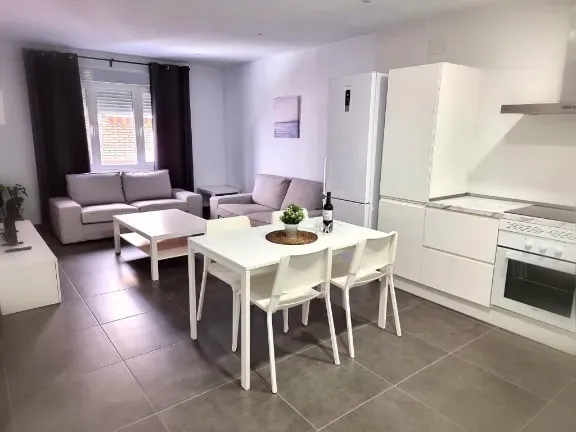 Espacio habitable moderno de concepto abierto con cocina y comedor blancos, dos sofás grises y una mesa de café.