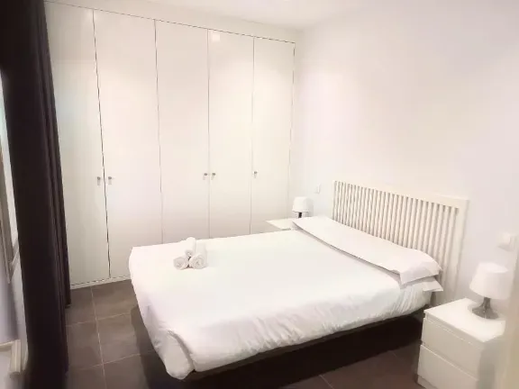 Dormitorio blanco con cama, mesitas de noche y armario. Espacio limpio y luminoso.