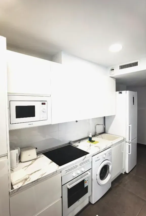 Cocina blanca con electrodomésticos que incluyen microondas, estufa, horno, lavadora y refrigerador.