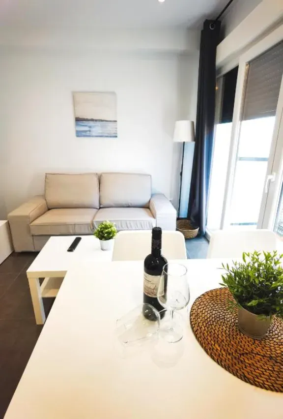 Sala de estar con sofá, mesa para dos, botella de vino y planta en maceta.