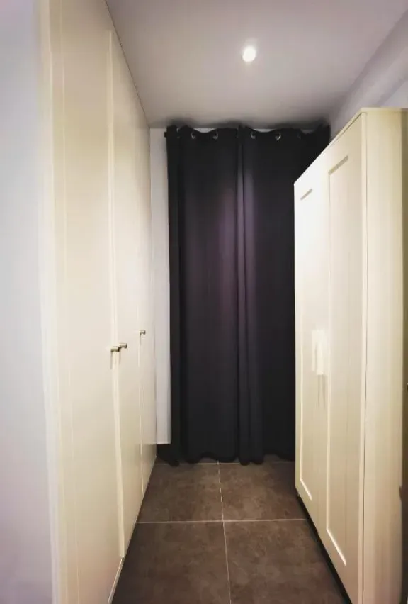 Pasillo estrecho con armarios de color crema y una alcoba con cortinas de color gris oscuro.