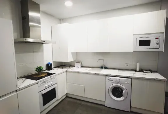 Cocina moderna blanca con electrodomésticos: vitrocerámica, microondas y lavadora. Encimeras de mármol.