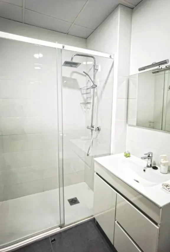 Baño blanco moderno con ducha de cristal, lavabo y espejo.