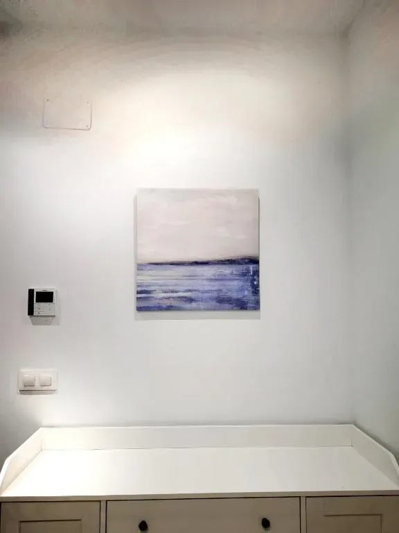 Pared blanca con una pintura abstracta azul y blanca, encima de un armario blanco.