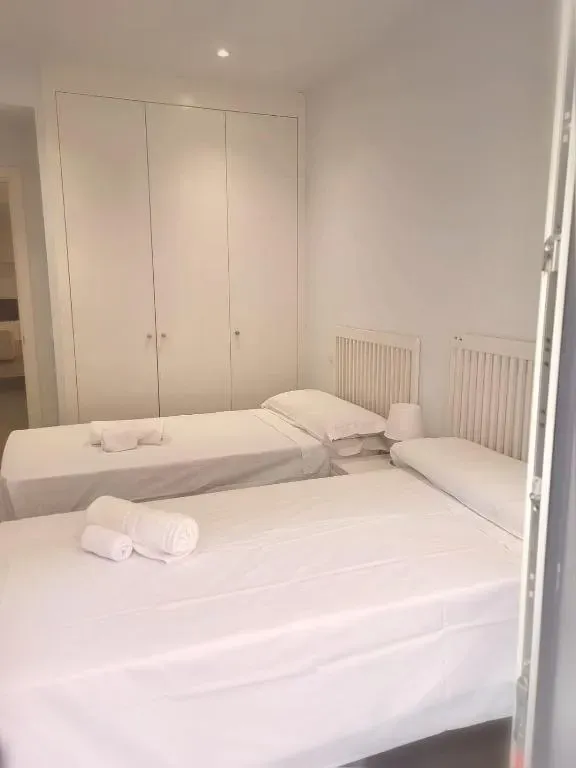 Dos camas individuales con ropa de cama blanca en un dormitorio luminoso. Armario blanco al fondo.