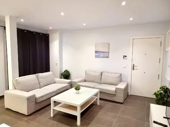 Sala de estar con dos sofás beige, mesa de centro blanca y plantas.