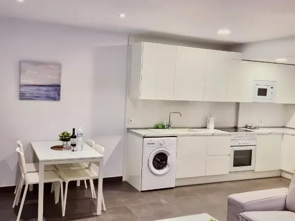 Cocina y comedor modernos de color blanco con electrodomésticos, mesa y sillas.