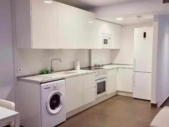 Cocina blanca con electrodomésticos que incluyen lavadora, refrigerador, microondas y estufa.