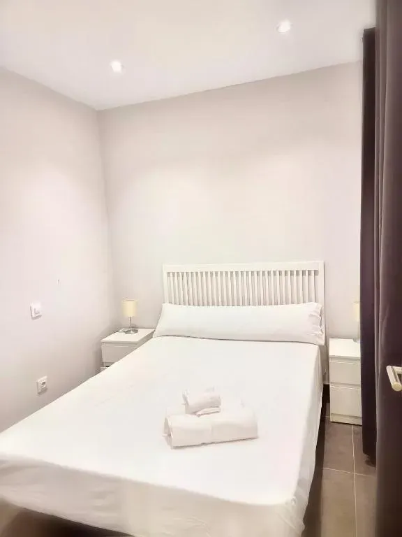 Dormitorio con cama blanca, dos mesitas de noche y una puerta marrón cerrada a la derecha.