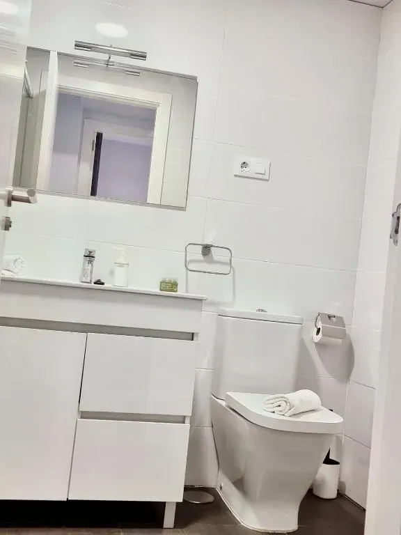 Baño blanco con tocador, inodoro, espejo y toallero.