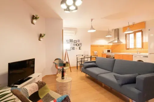 Combinación de sala de estar y cocina, con un sofá azul, detalles en naranja y elementos decorativos.