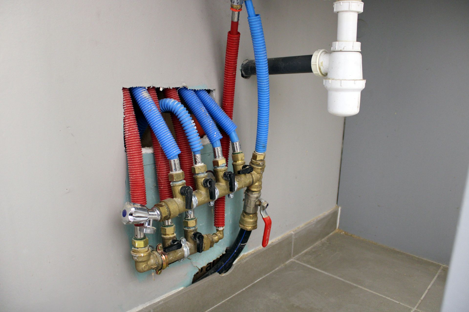 Collecteur de plomberie avec tuyaux et vannes rouge et bleu contre un mur à côté d'un tuyau d'évacuation blanc.
