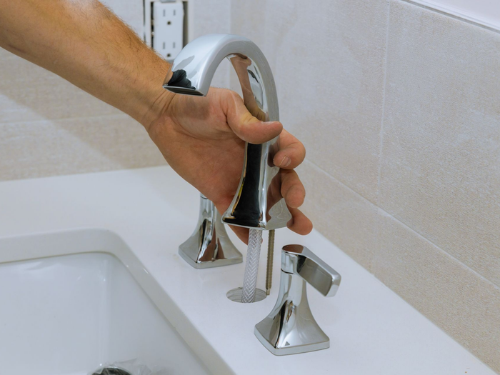 Réparation d'un robinet de lavabo chromé près d'un lavabo blanc.