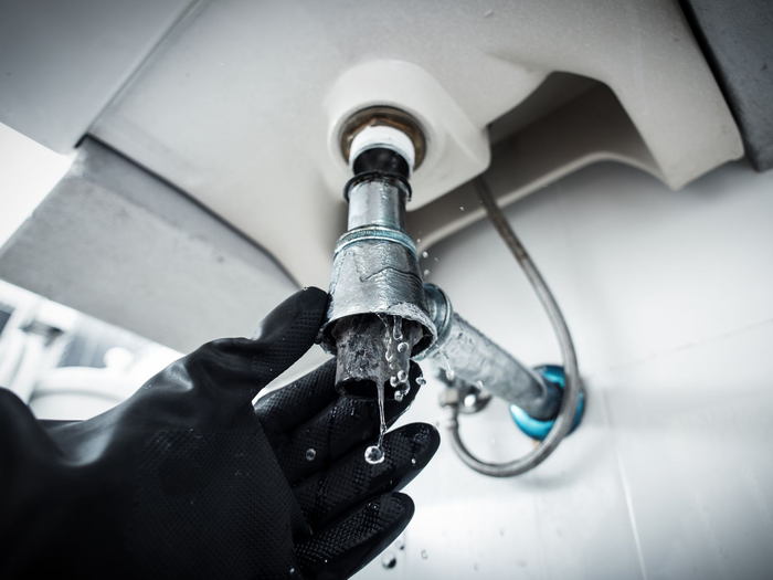 Main gantée réparant une fuite d'évier sous un robinet de salle de bain.