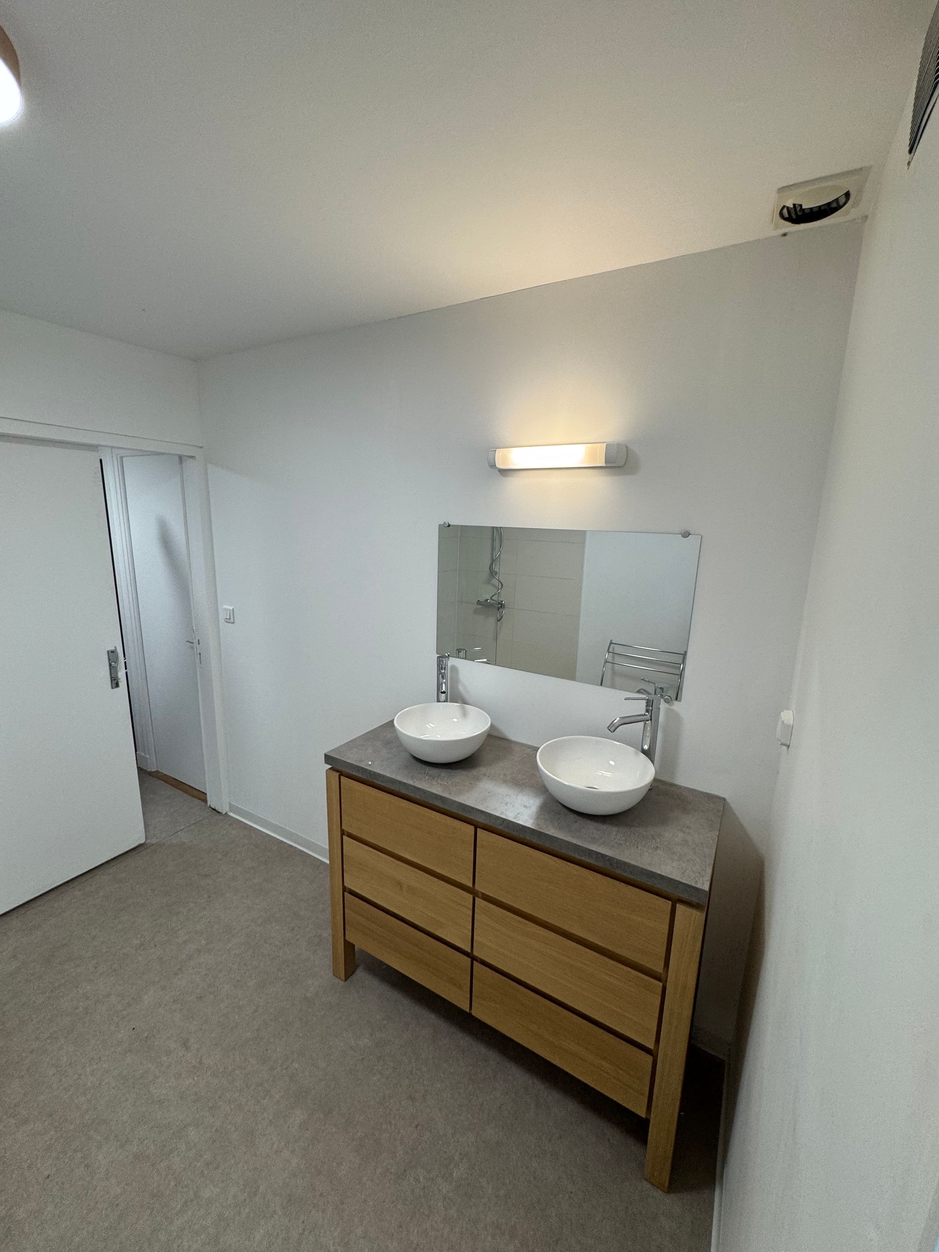 Lavabo avec deux vasques blanches, miroir, applique murale et porte de placard sur la gauche.