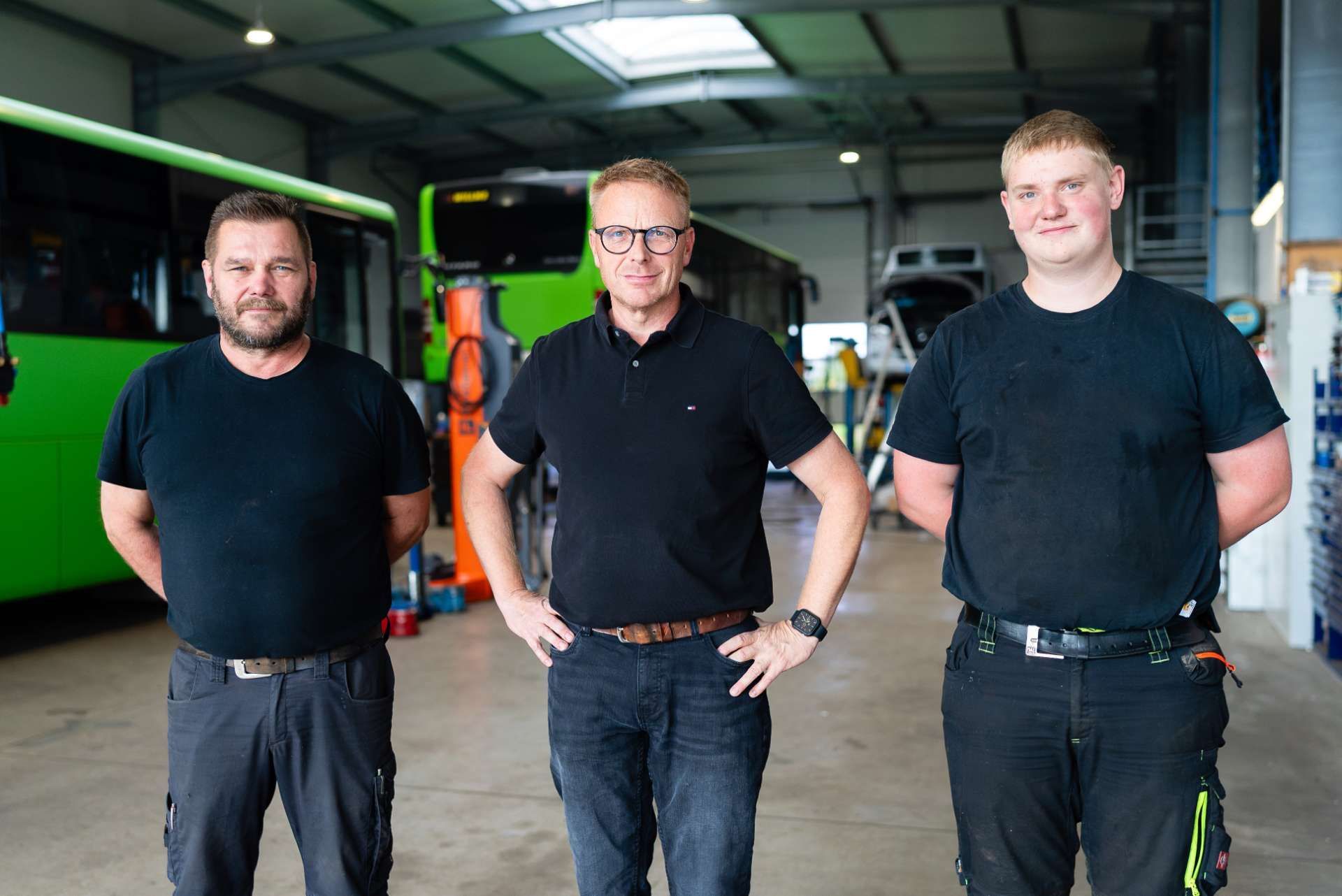 Das Team  in Arbeitskleidung posiert in einer Garage mit einem Lastwagen und einem Bus.