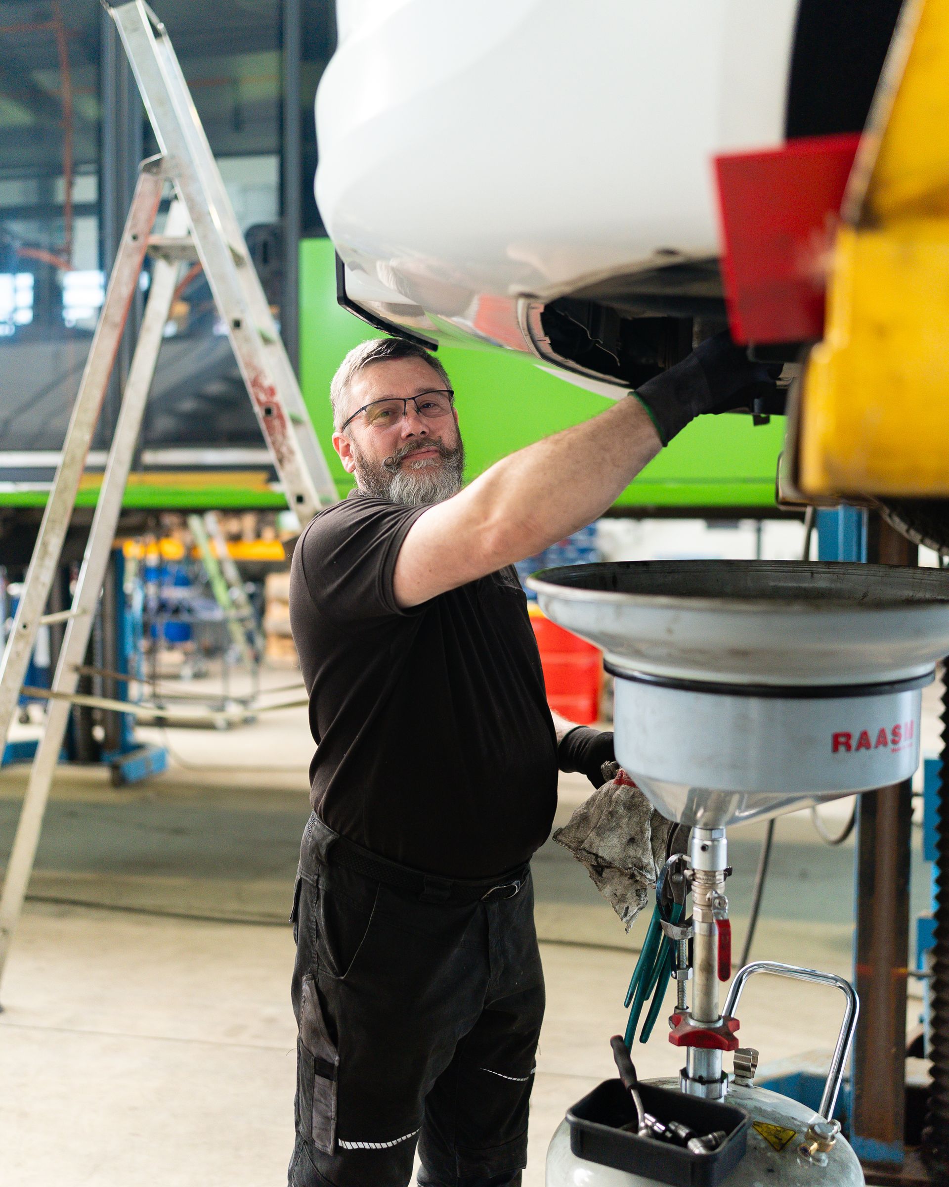 Ein Mechaniker in blauem Overall untersucht einen Automotor und macht sich Notizen auf einem Klemmbrett.
