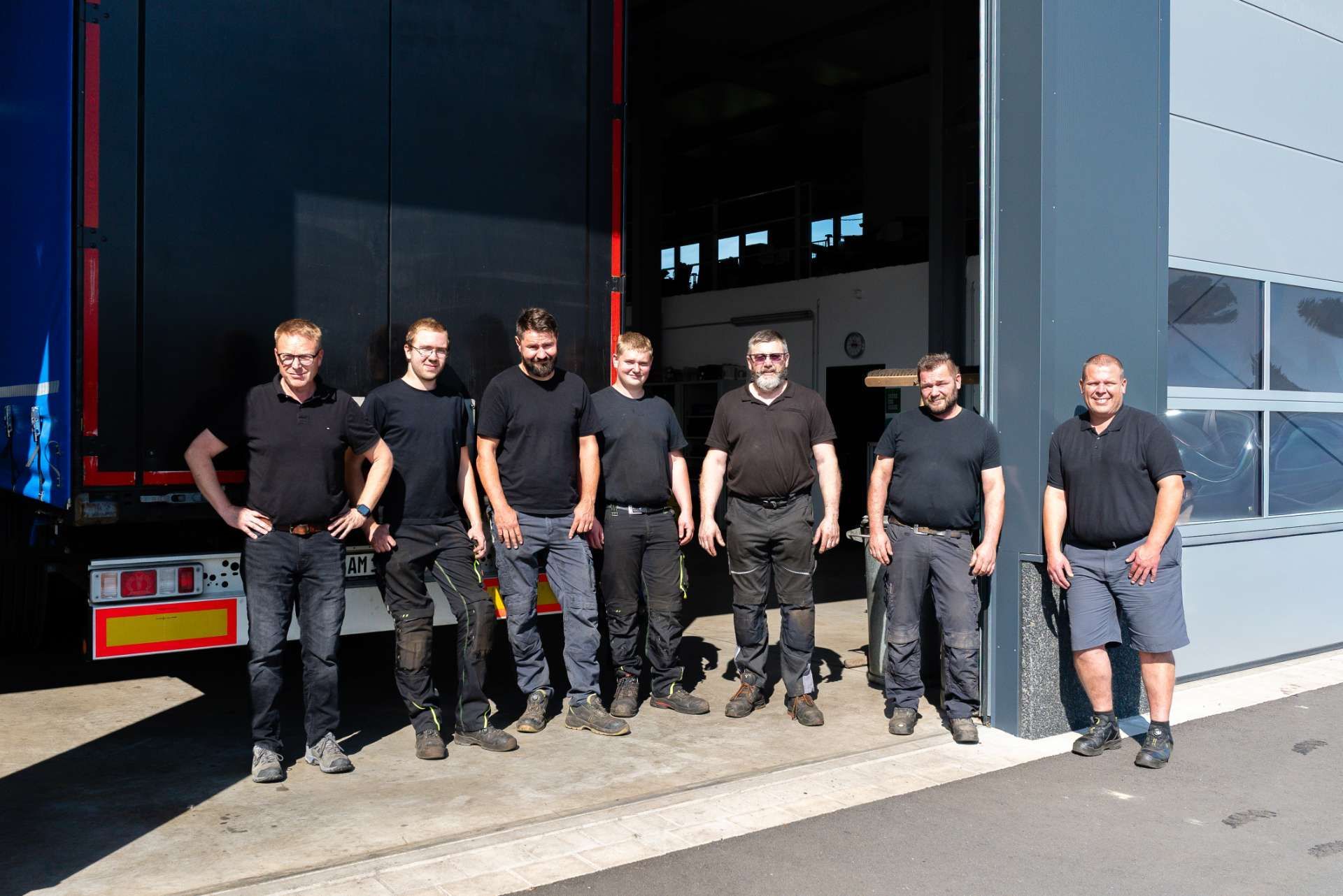 Das Team  in Arbeitskleidung posiert in einer Garage mit einem Lastwagen und einem Bus.